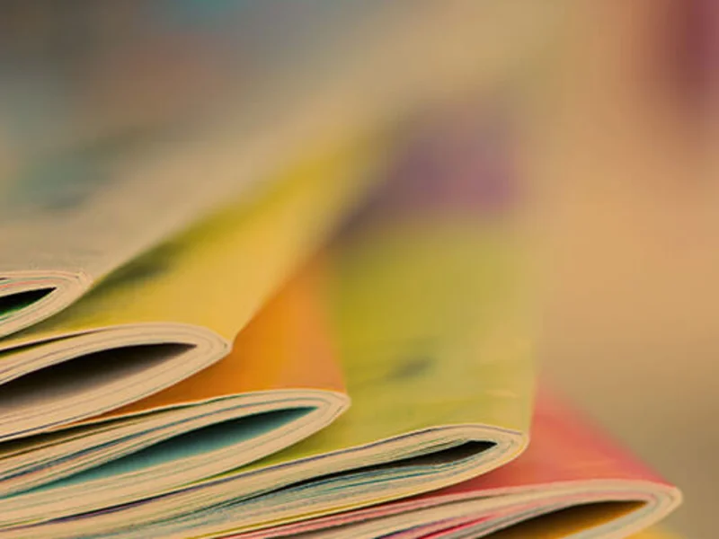 Nahaufnahme eines aufgefächerten Stapels bunter Magazine mit orange, gelb und rosa gefärbten Seiten.